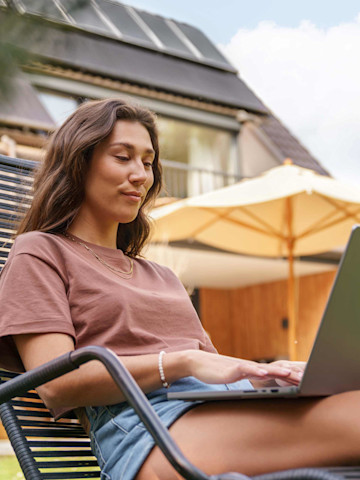 Frau am Laptop im Garten im Hintergrund Dach mit Solaranlage