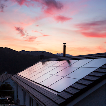 Solarmodule auf einem Dach nach Sonnenuntergang mit Hügeln und rötlichem Himmel im Hintergrund.