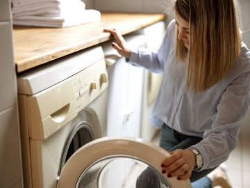 Frau befüllt die Waschmaschine mit Wäsche