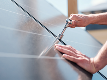 LichtBlick Fachpartner befestigt Solarmodul auf einem Dach mit einem Werkzeug.