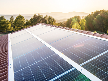 Solarmodule auf einem Dach mit silberfarbenen Rahmen bei Sonnenaufgang mit Bäumen und Hügeln im Hintergrund.