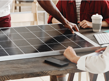 Drei Personen stehen um einen Tisch auf dem ein Solarmodul liegt und planen das passende LichtBlick Solar-Komplettpaket.