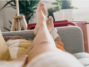 Frau liegt entspannt auf dem Sofa, man sieht nur den nackten unteren Teil der Beine und die Füße aus Sicht der Frau.