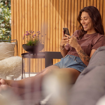Frau sitzt auf einer Couch und nutzt die LichtBlick App auf dem Smartphone.
