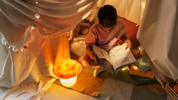 Junge liest Buch in selbstgebautem Zelt
