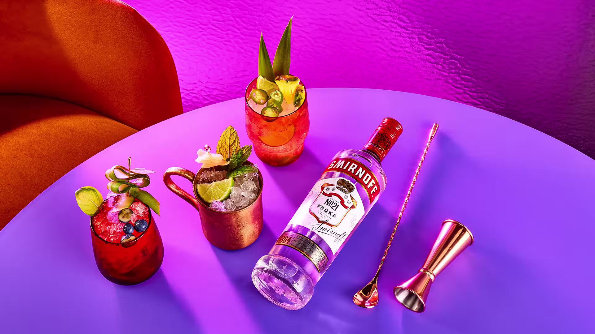 A bottle of Smirnoff 21 laying on a table next to three Moscow Mules