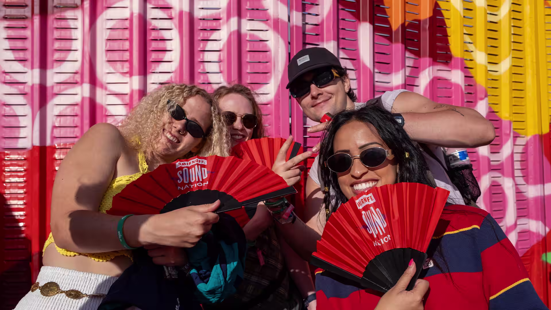Festivalgoers smiling with red Smirnoff Sound Nation folding fans in front of a colourful backdrop reading Community.
