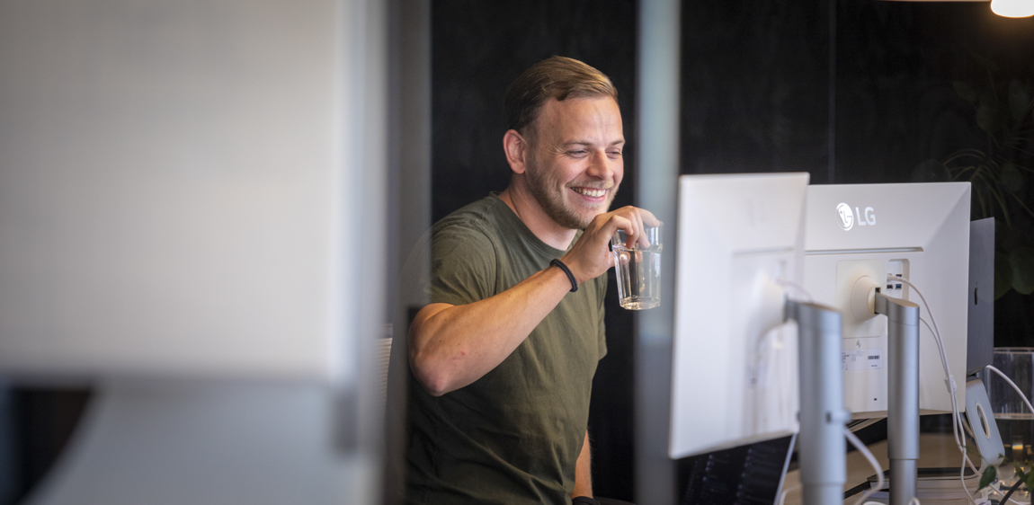 Een developer (Ronald) drinkt water en staat voor zijn bureau.