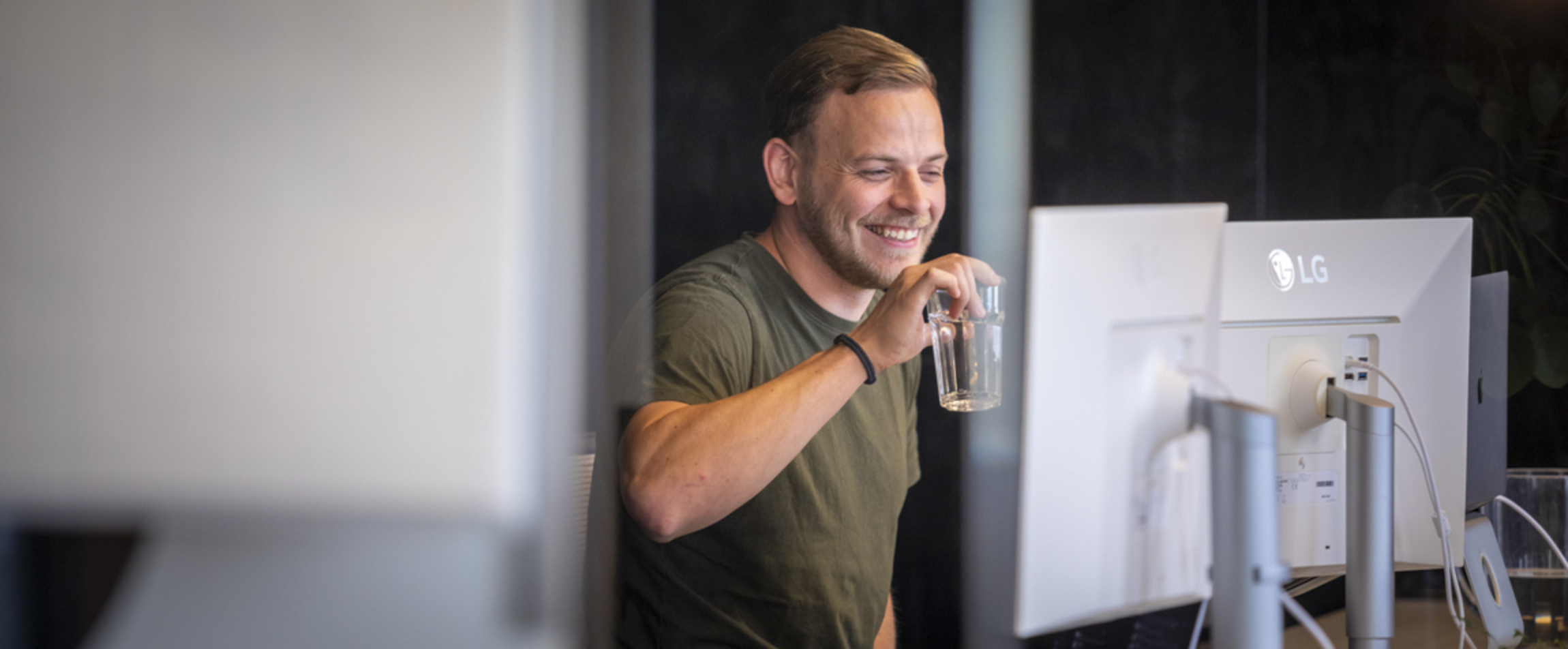 Een developer (Ronald) drinkt water en staat voor zijn bureau.