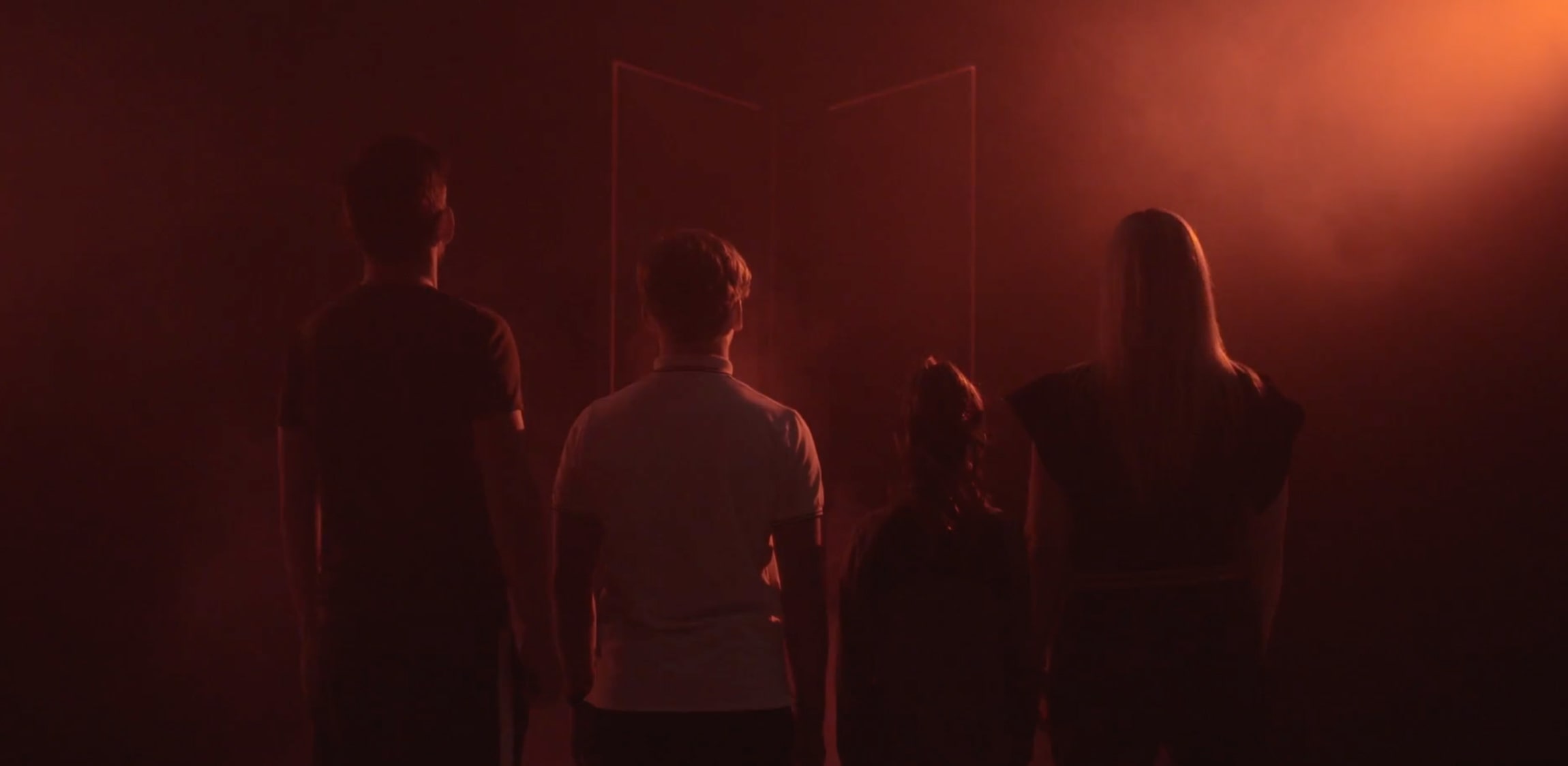 Een donkere foto met vanaf de rechtse bovenhoek een rode gloed die ervoor zorgt dat je de silhouetten van een familie ziet. 