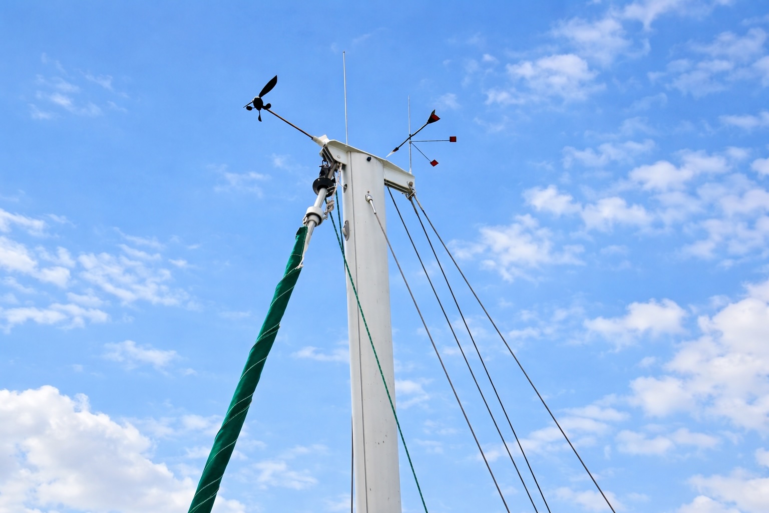 The top of a sailboat mast with an electronic wind sensor and a traditional wind vane.