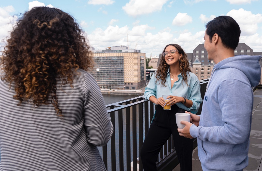 Drei Personen - zwei Frauen und ein Mann - unterhalten sich auf einem Balkon an der Spree in Berlin. Eine Frau lächelt.