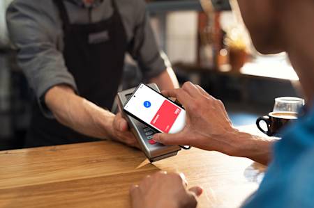Ein Mann wird dabei beobachtet, wie er mit der Lexware Card Wallet App auf seinem Mobiltelefon eine Zahlung an einen anderen Mann vornimmt.