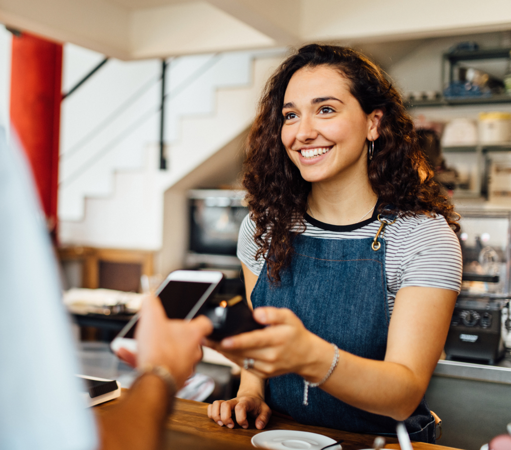 Picture of woman smiling while she collects card payment of a customer with a POS. 
