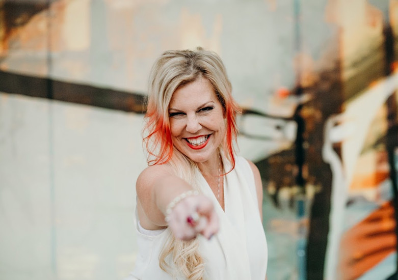 Portrait of Janelle Hoyland smiling and pointing at the camera.