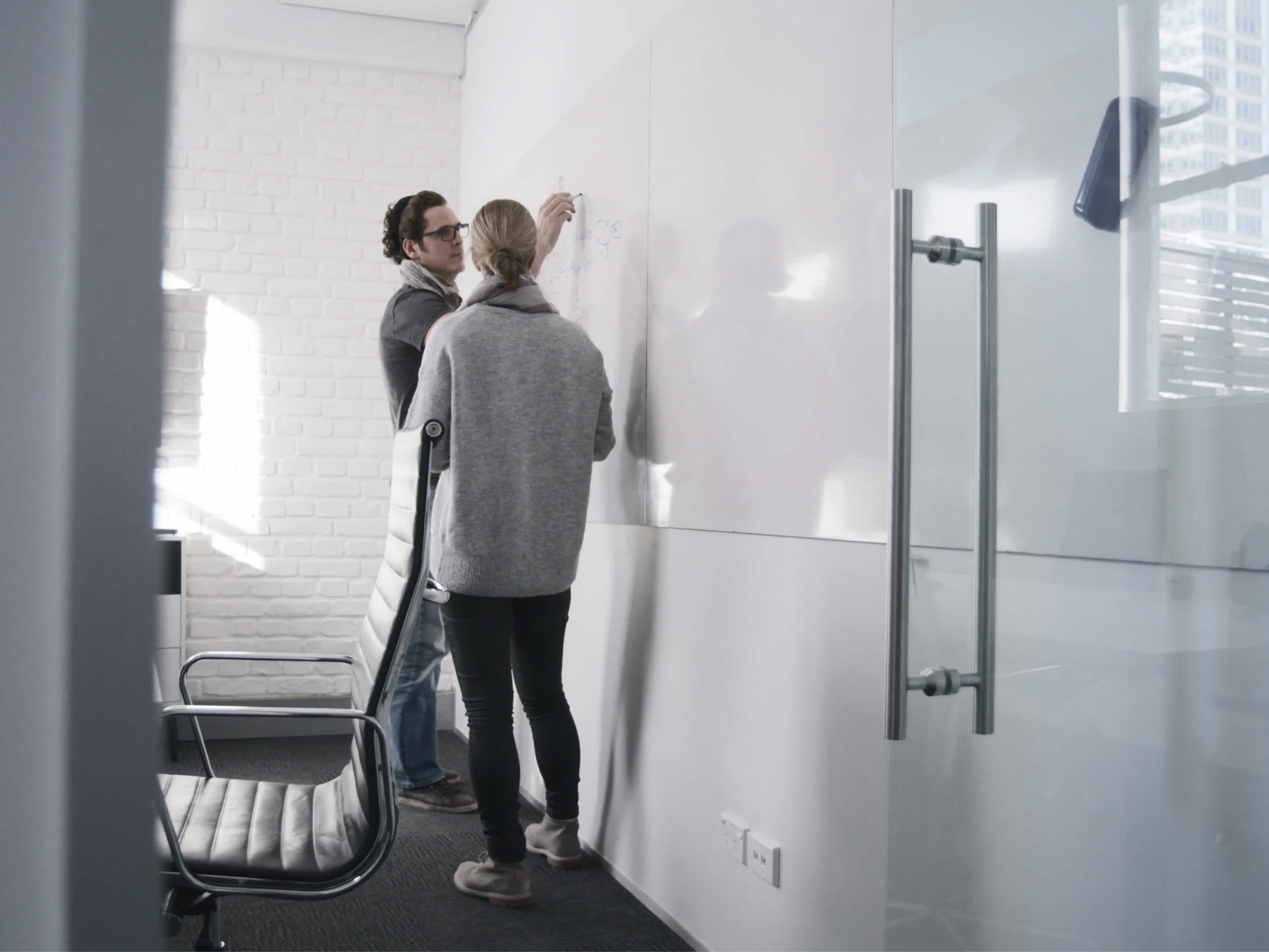 Two individuals sharing ideas over a whiteboard