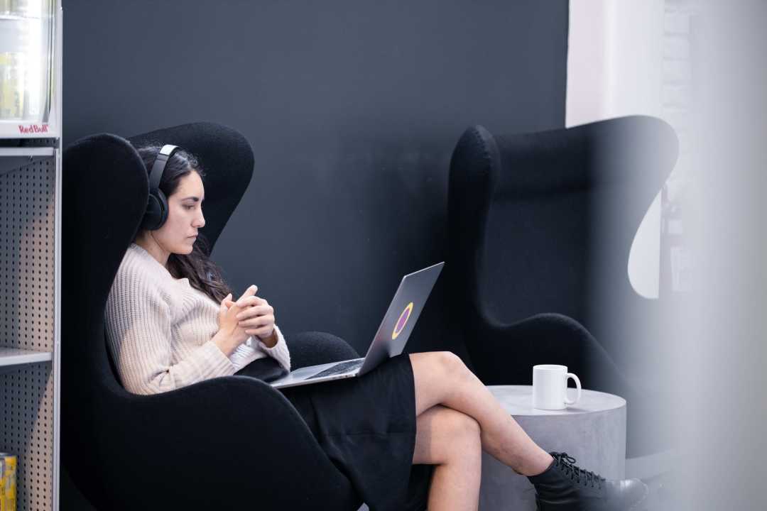 A photograph of a woman using her computer with headphones on