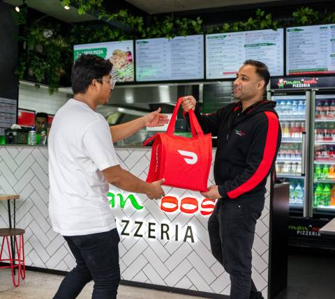 Manoosh Pizzeria employee hands a Dasher a DoorDash bag