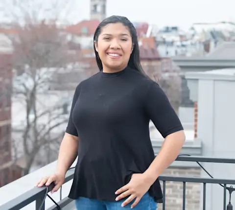 Person in black top smiling on balcony with urban cityscape in background on a winter day.