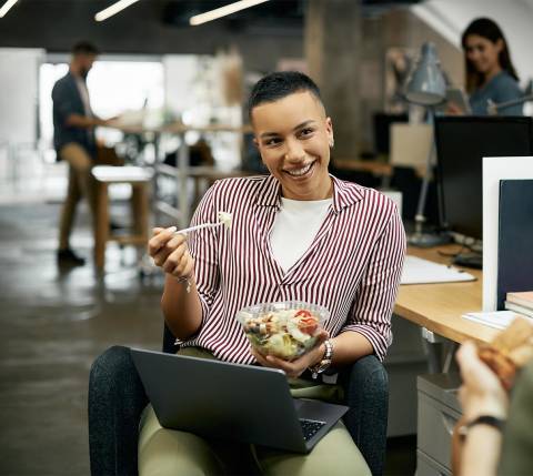 DDfB - Blog - How Eating Healthy at Work Can Improve Performance - Smiling employee with meal and laptop