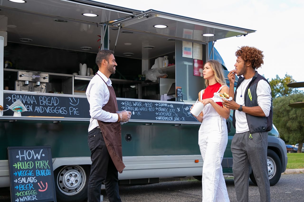 Customers enjoying fast food at an outdoor food truck with a friendly server.
