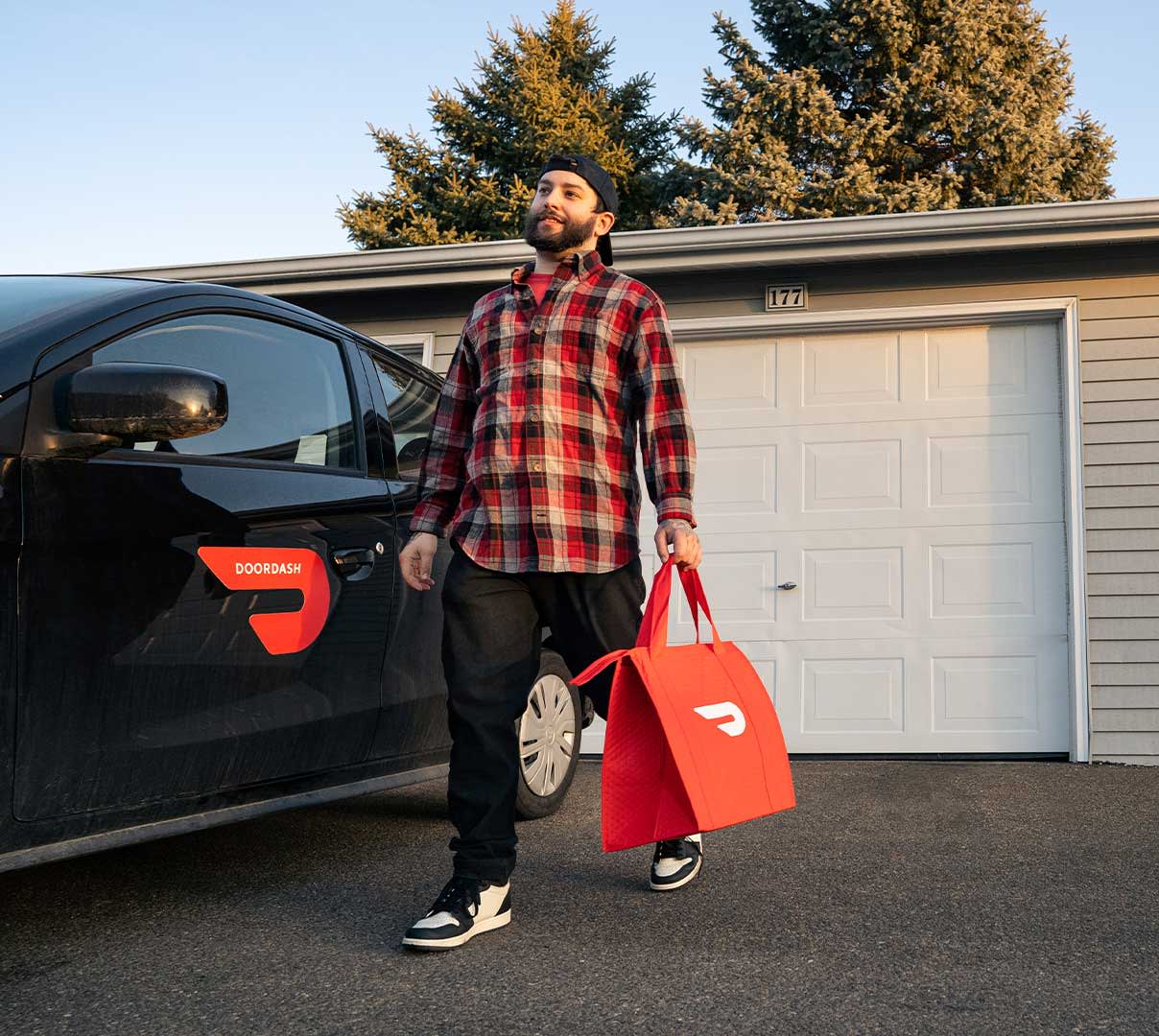 Male Dasher carrying large DoorDash bag in front of car