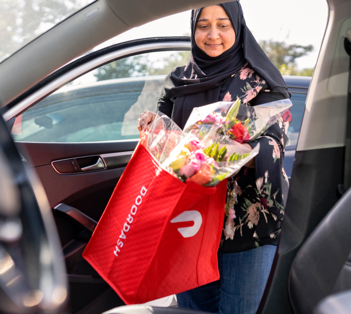 Woman exiting car with DoorDash bag of flowers