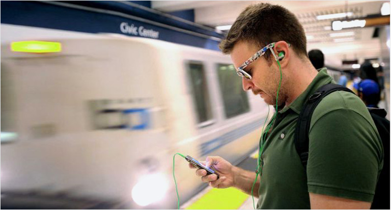 subway wifi-guy standing in a subway looking at his phone with earbuds in.