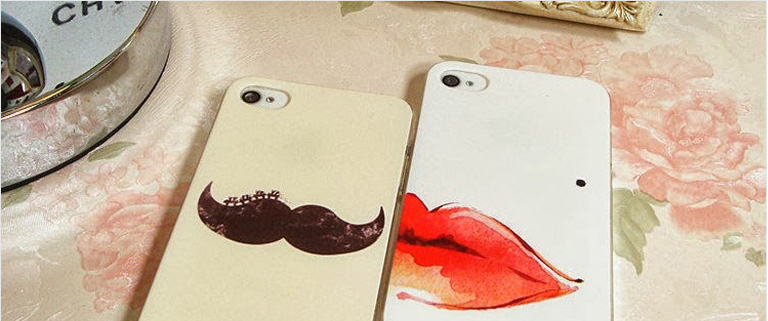 love apps-two iPhones on a table, left one has a mustache on its case the right on has a red lips on its case.