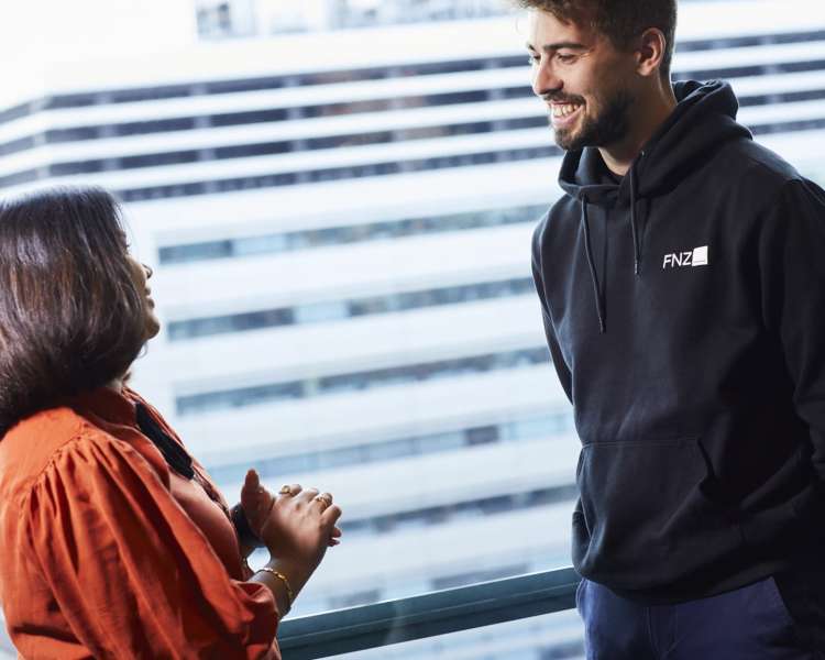 man in a black FNZ hoodie talks with a woman