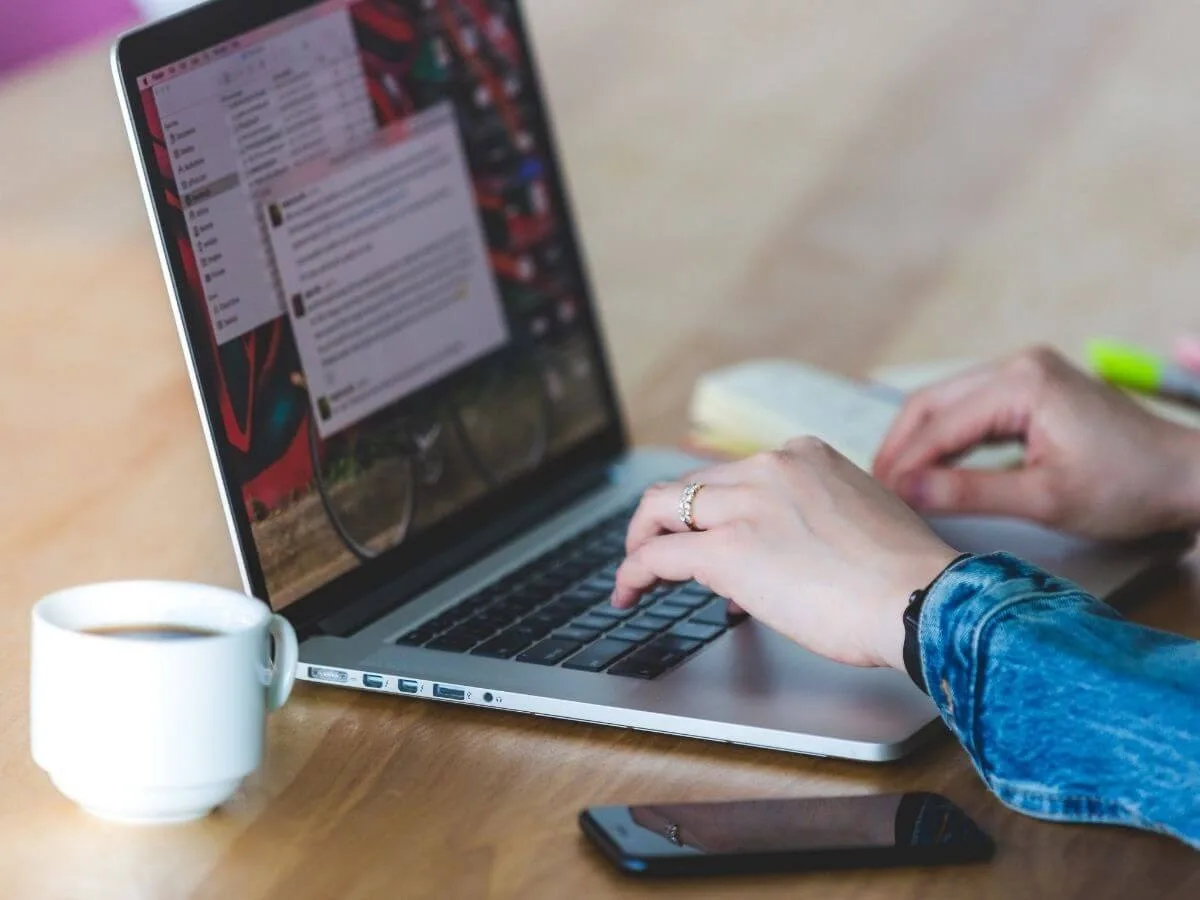 person typing on a laptop with a smartphone and coffee cup nearby