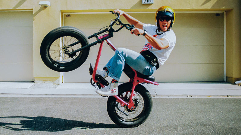 Guy wearing a helmet on a Super73 Z Miami while doing a wheelie.