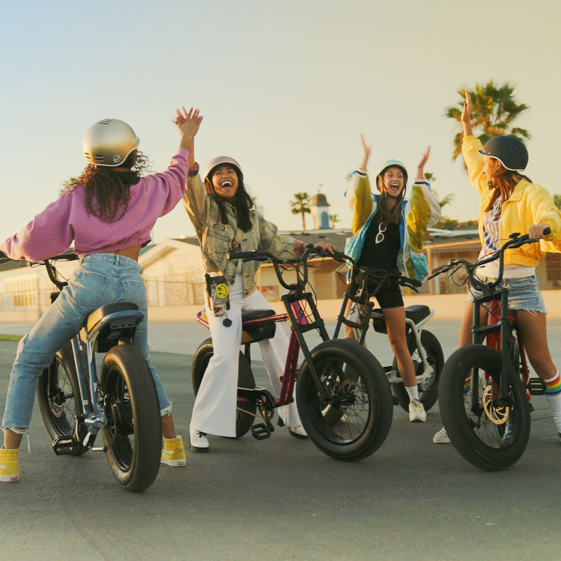 Four young friends high-fiving and wearing helmets while sitting on the Super73-Z Miami.