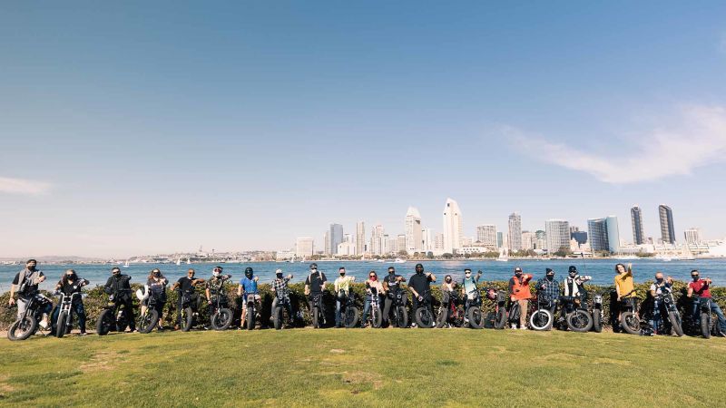 A shot of 15 Super Squad members lined up with their bikes against the Long Beach, CA skyline.