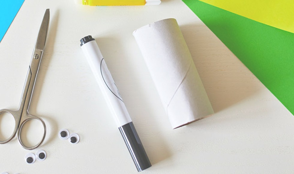 A pair of scissors, a black marker and an empty paper toilet roll laying on the table.