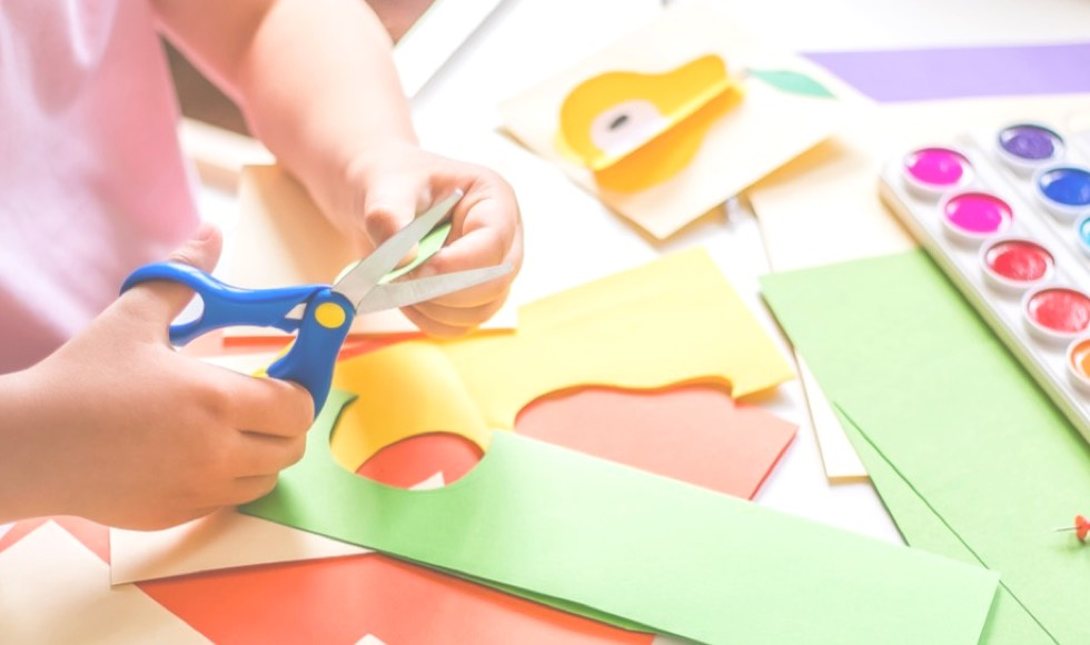 Young girl using a pair of scissors to cut a piece of construction paper