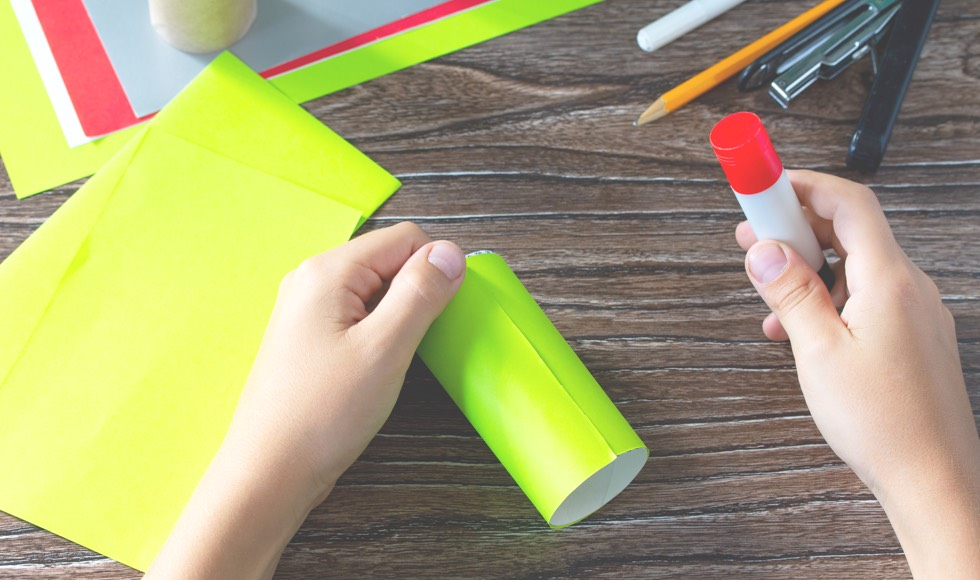 Hand holding glue stick and paper towel roll