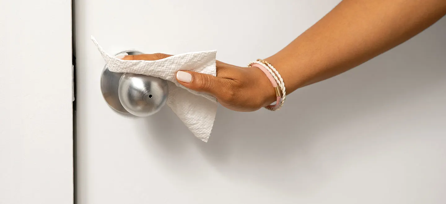 Une main de femme nettoie une poignée de porte avec l'essuie-tout Bounty