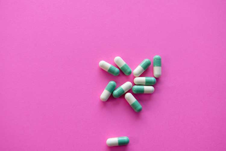 Green and white capsules to represent acyclovir pills on pink background.