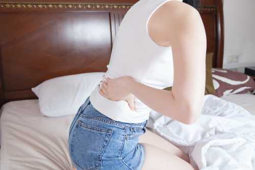 Woman grabbing her back in pain—norethindrone can help to delay your period.
