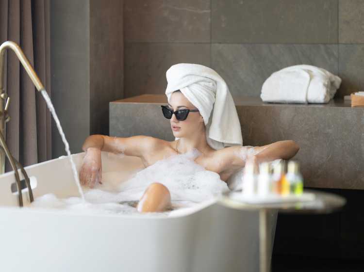 Girl wearing sunglasses and a towel on her head taking a luxurious bath with Balancing Wash