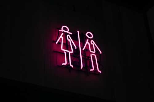 A pink neon washroom sign with two line figures.