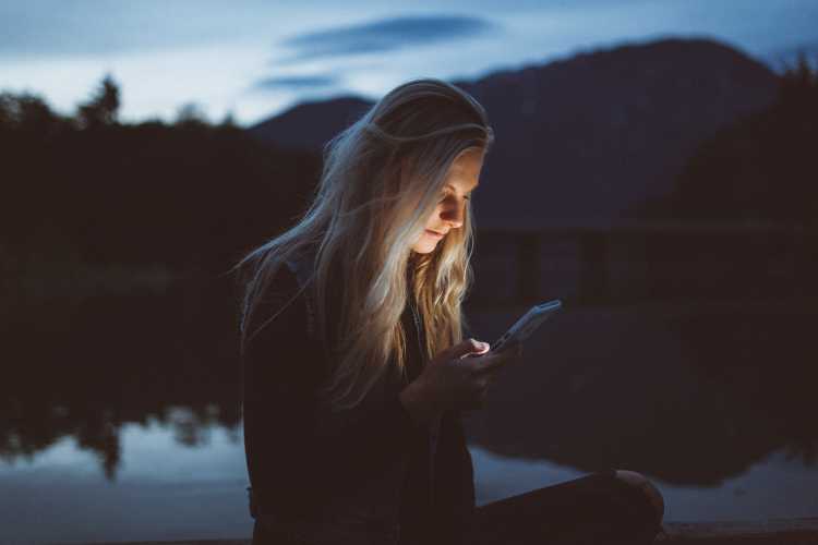 Woman learning about online abortion from her phone outside at dusk.