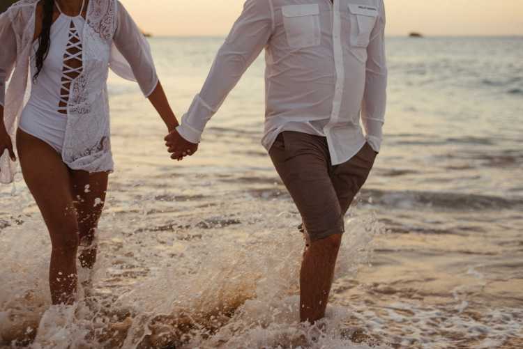 A couple walked on the beach holding hands and wearing white—she used a pill to delay her period.