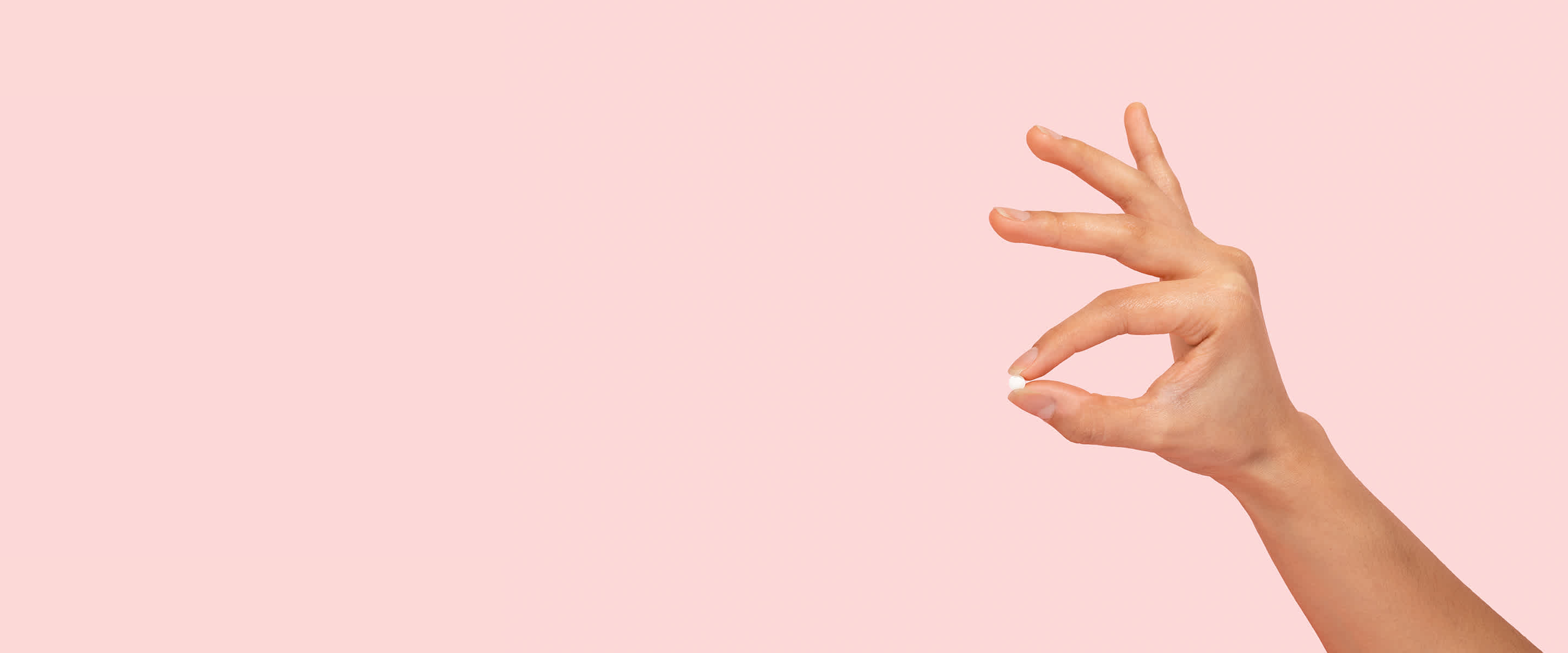 A hand holding a single emergency contraception pill between the thumb and index fingers.