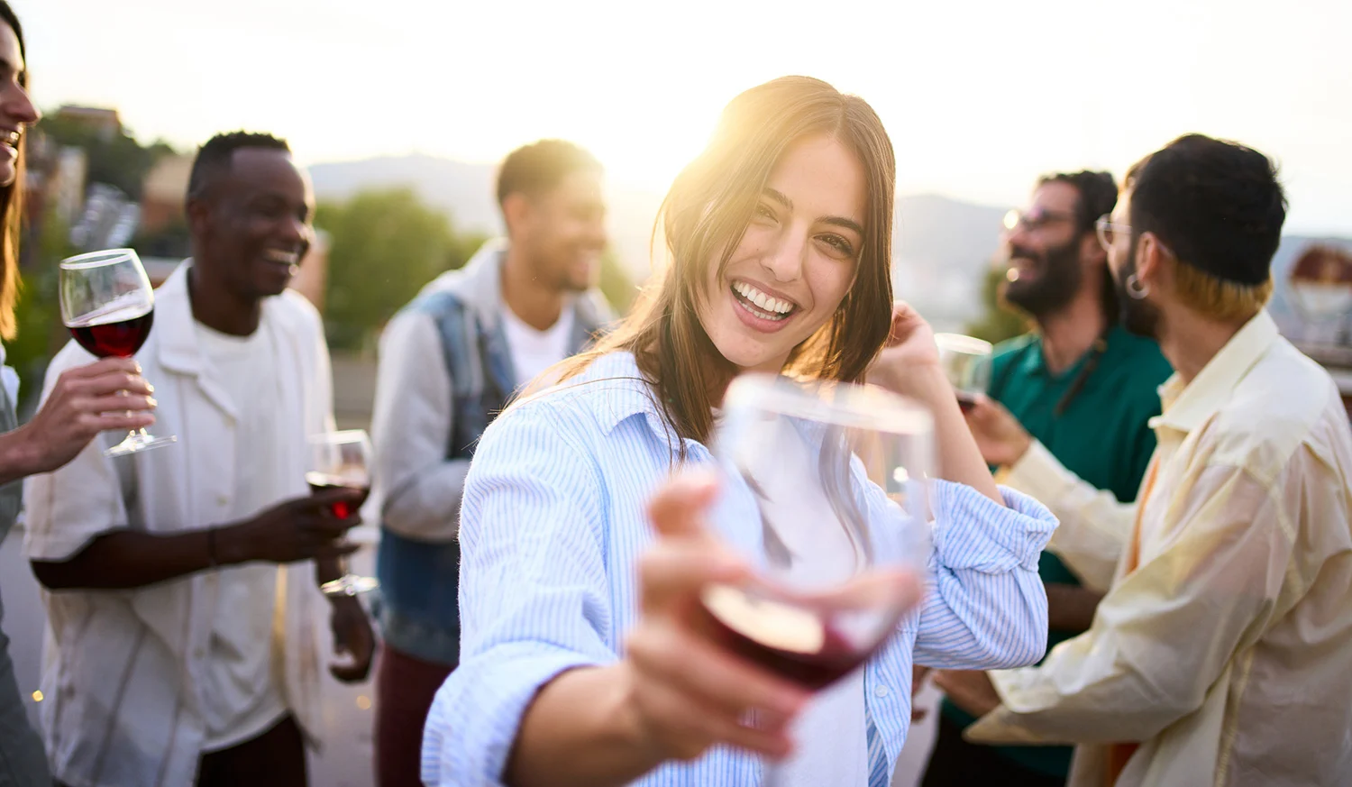 Titelbild Junge Frau, die mit einem Glas Rotwein in der Hand in die Kamera schaut und lächelt