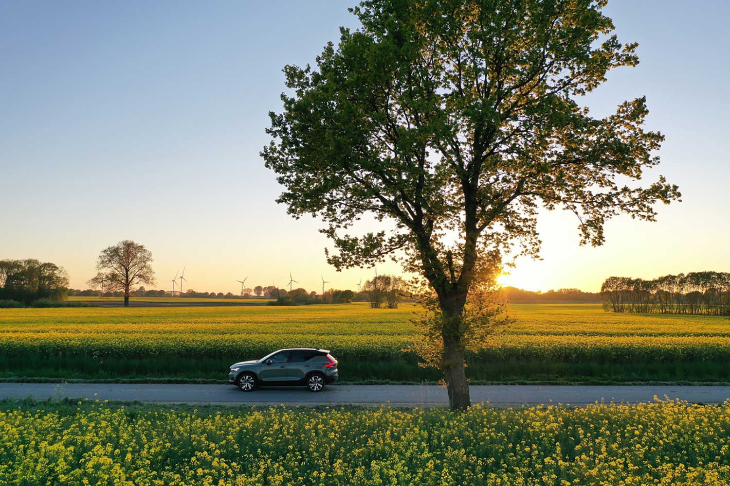 Elektroauto fährt in der Natur mit Windrädern im Hintergrund