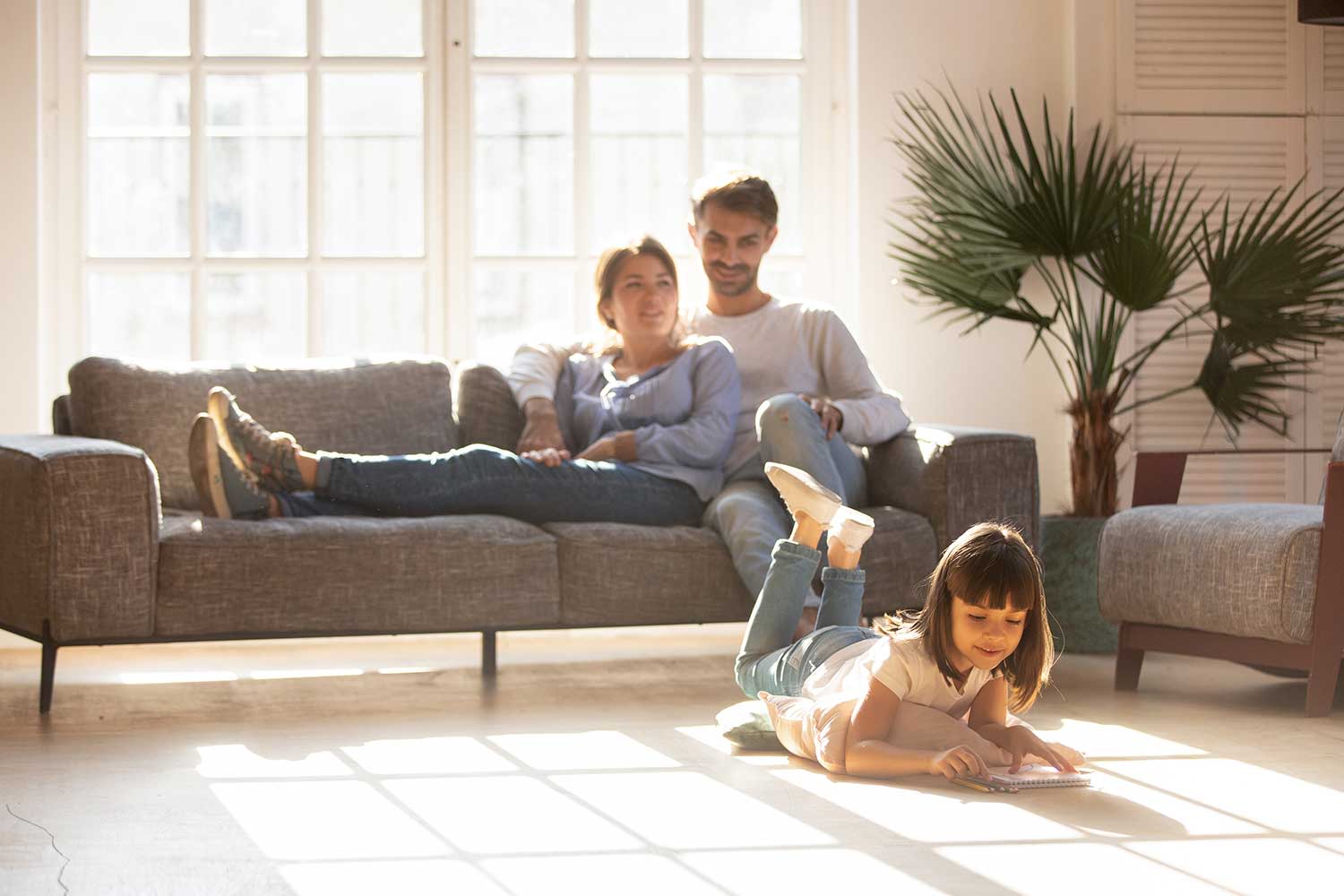 Glückliche Eltern entspannen sich auf der Couch, während die Tochter auf dem Boden zeichnet