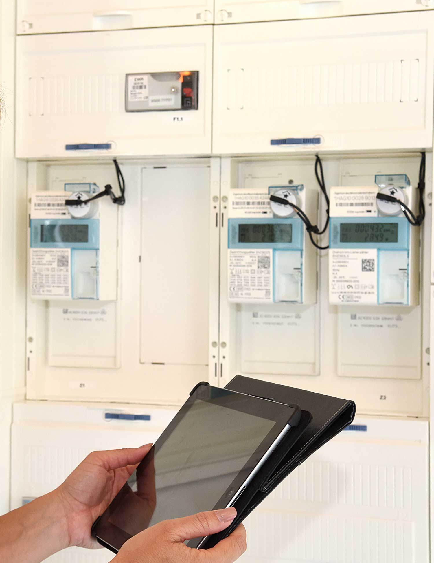 Zwei Hände halten ein Tablet vor einem Zählerschrank. Zwei Hände halten ein Tablet vor einem Zählerschrank.
