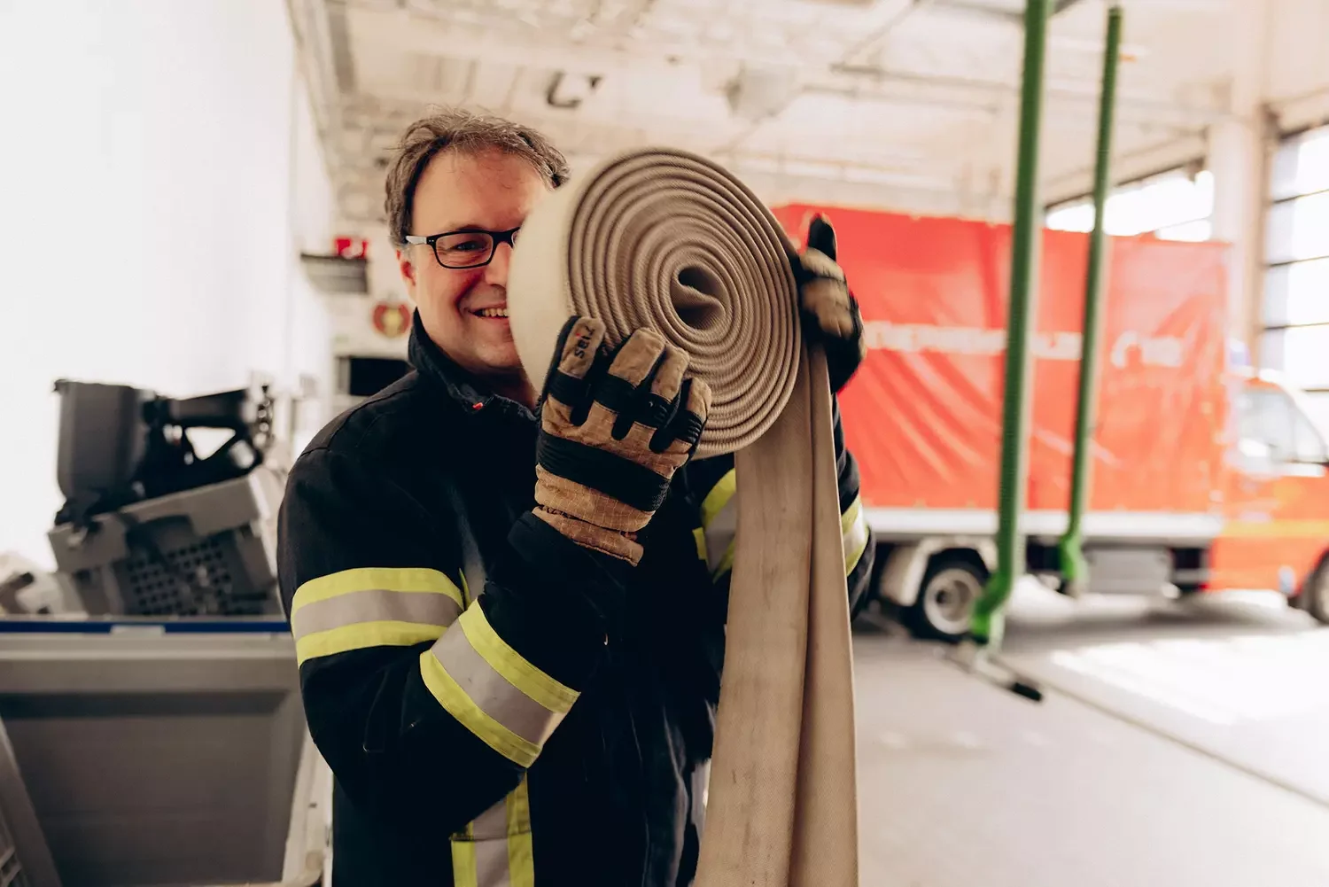 Glücklicher Feuerwehrmann mit Feuerwehrschlauch in der Hand.
